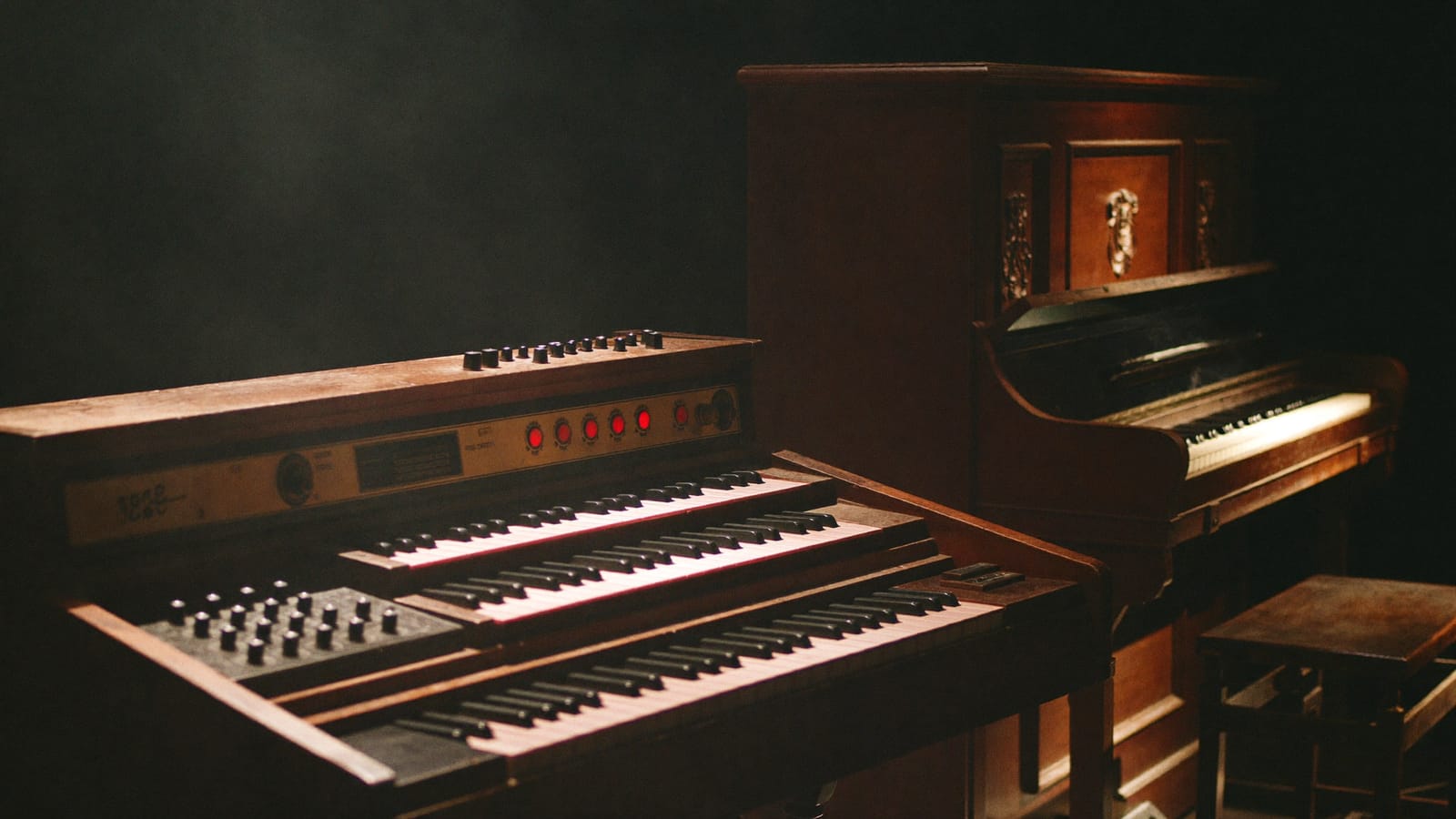 A vintage 1960s combo organ and electric piano on a dark stage under a tungsten spotlight