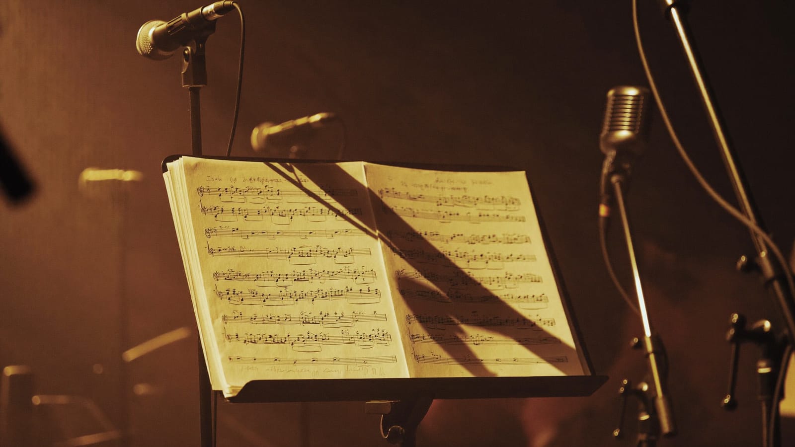 Vocal harmony charts on a music stand under warm stage light with vintage microphones behind